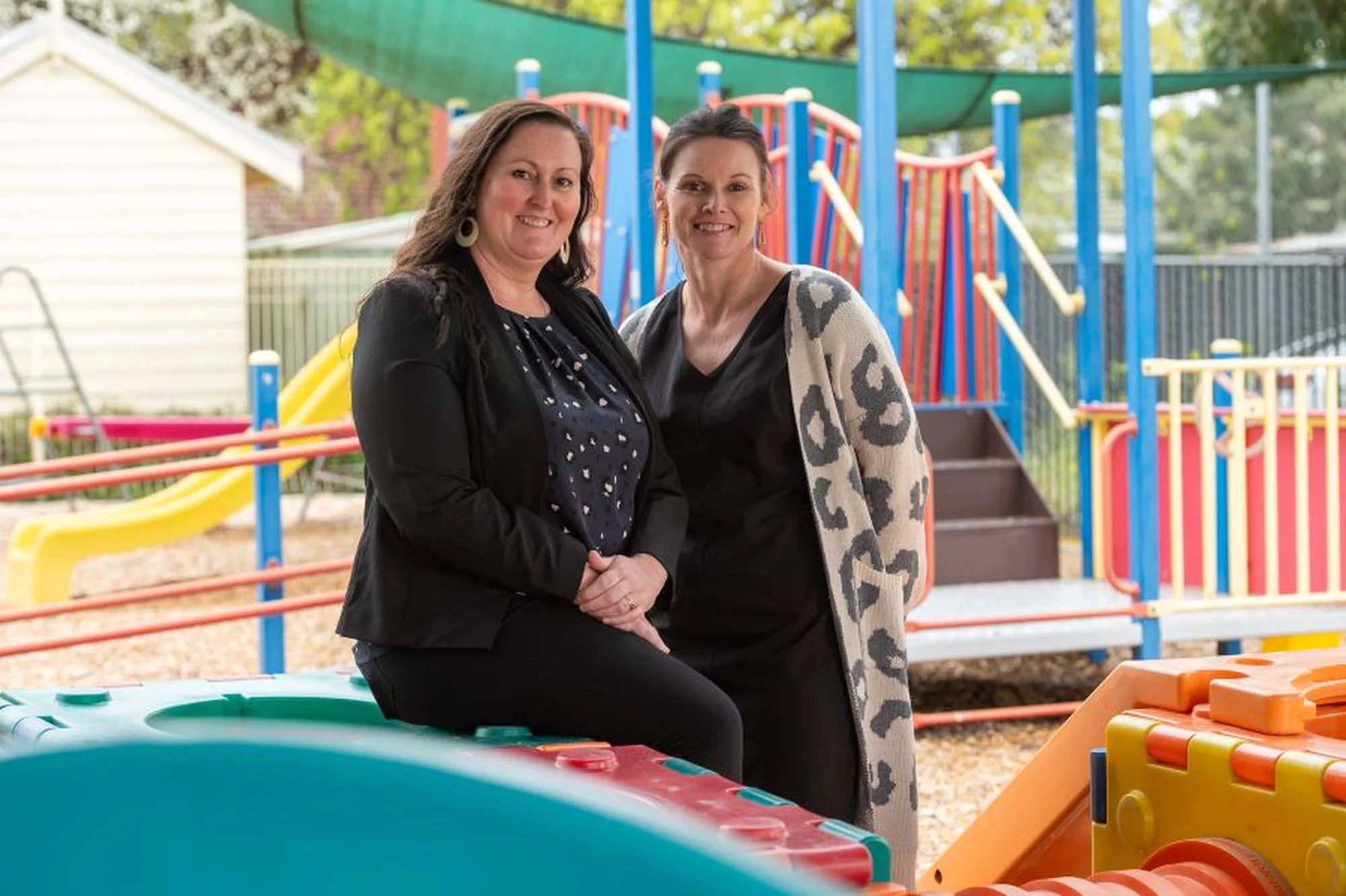 Two smiling BCHS team members in front of a colourful playground